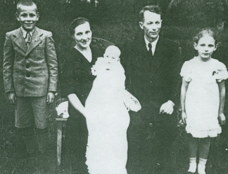 Karline holding baby Ausma in her christening gown, with family standing by.