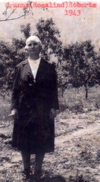 Woman standing in a field, trees behind her. 
