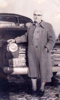 Woman wearing glasses leaning against an old car.