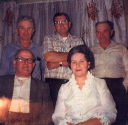 Colour photograph of a man and a woman, seated, three men standing behind them.