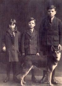 Portrait of three children in dark clothes, a dog in front of them.