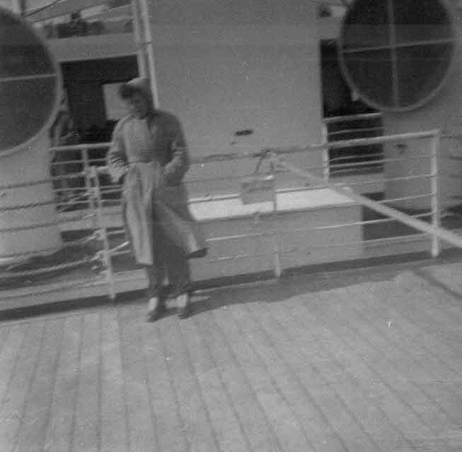 Man is standing on the upper deck of the ship holding over coat.