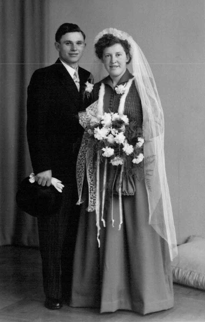 Couple in wedding dress standing infront of wall holding flowers in hand.