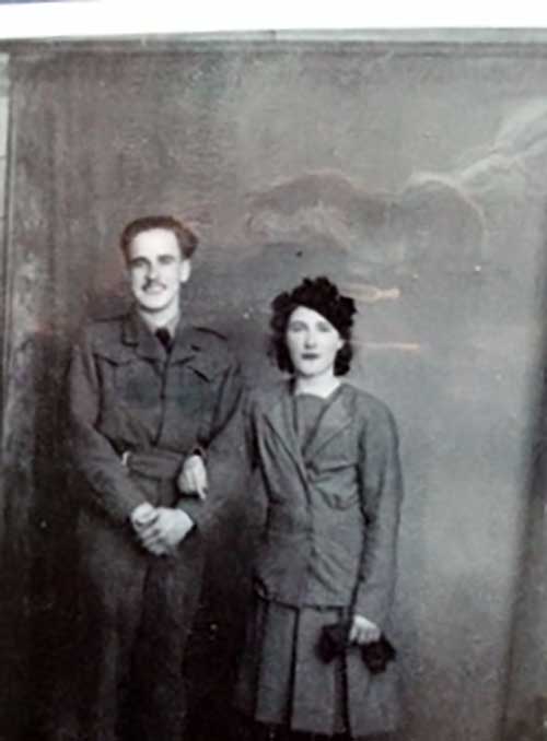 A man and woman stand in front of a wall to have their photo taken.
