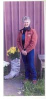 Color photograph of a woman standing next to a flowerpot in the shape of a boot. 