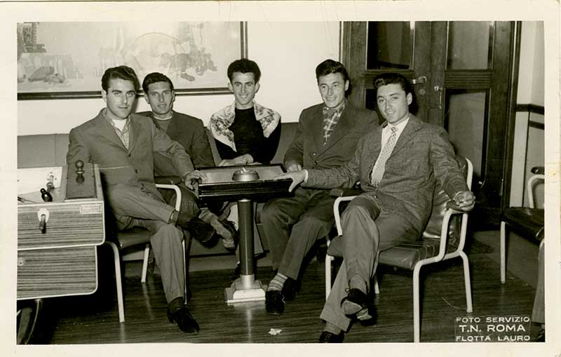 Five young men sit around a table and pose for a professional photograph.
