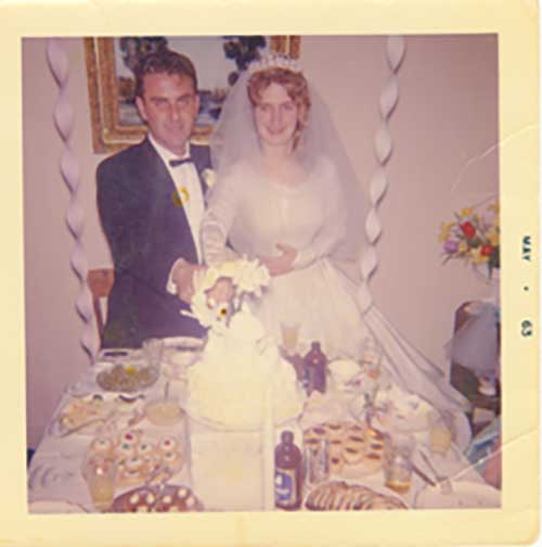 A bride and groom stand in front of a table laden with lots of food and a wedding cake.