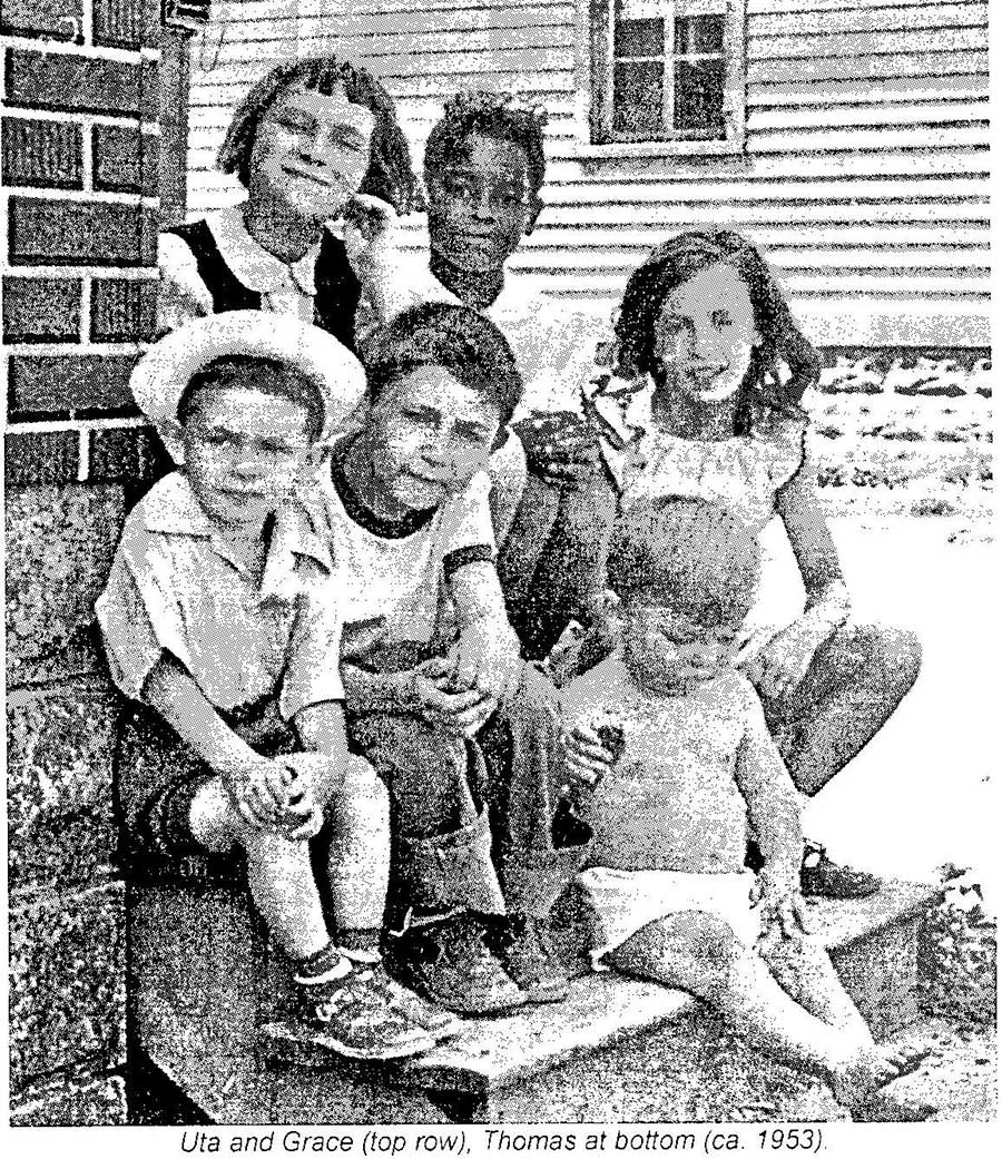 A black and white photo of six children sitting outside together on steps and smiling at the camera.