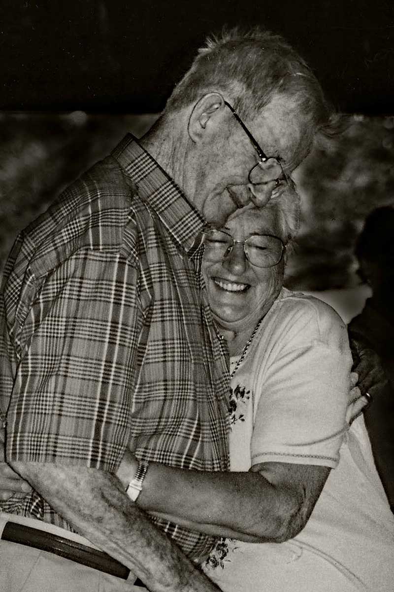 A man holds his wife in a loving embrace and she is smiling broadly.