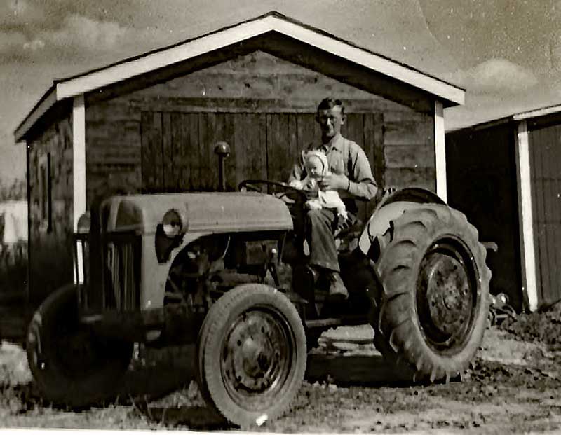 A young man holds a baby while sitting on a tractor.