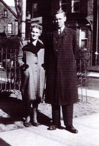 Man and woman in coats, standing on a street corner.