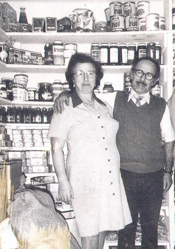 A man and woman stand in front of shelves full of canned food. 