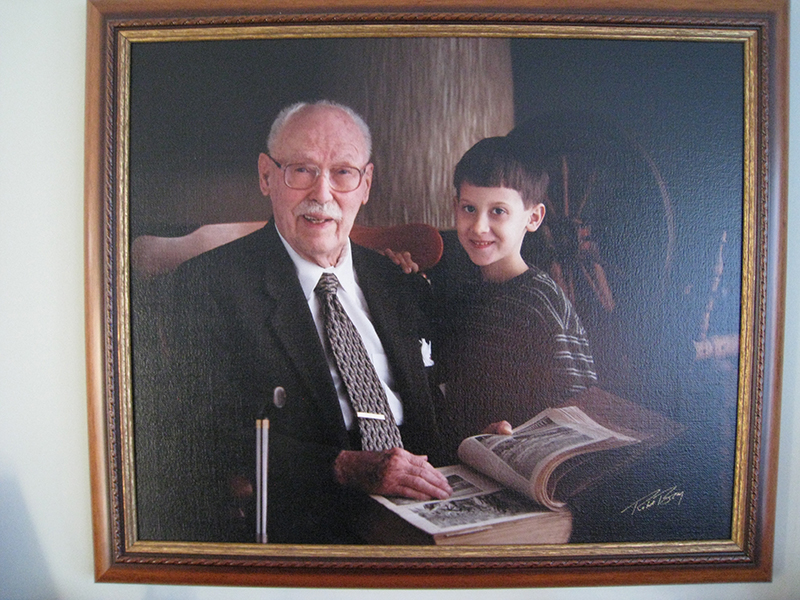 Framed painting of older gentleman with young boy, reading a book.