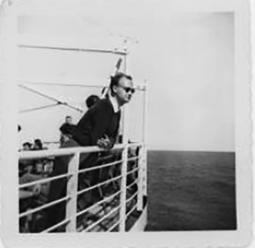 A man is leaning on the rail of a ship wearing sunglasses.