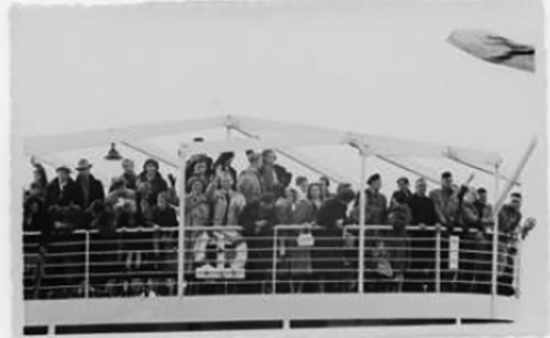 A large group of people stand close to the railing of the ship.