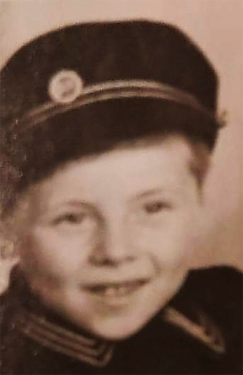A little boy wearing a cute cap and uniform smiles at the camera.