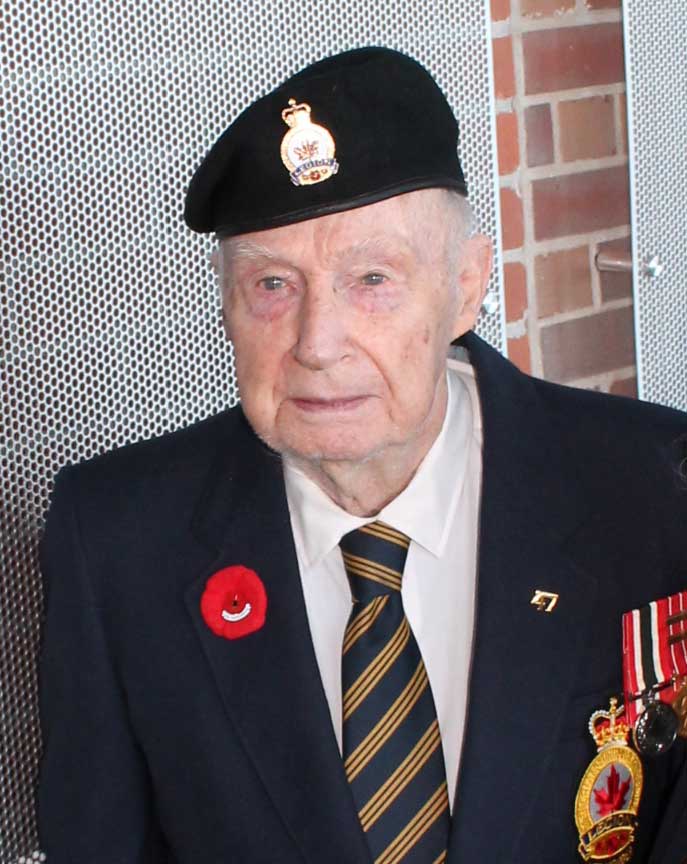 Veteran with military beret and medals stands in front of the Wall of Service,