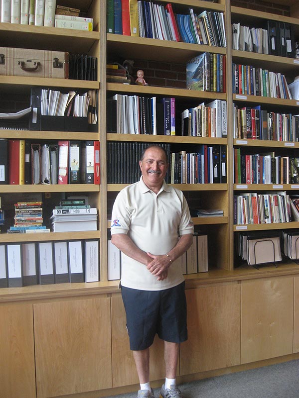 A smiling Italian man standing in front of bookshelves.