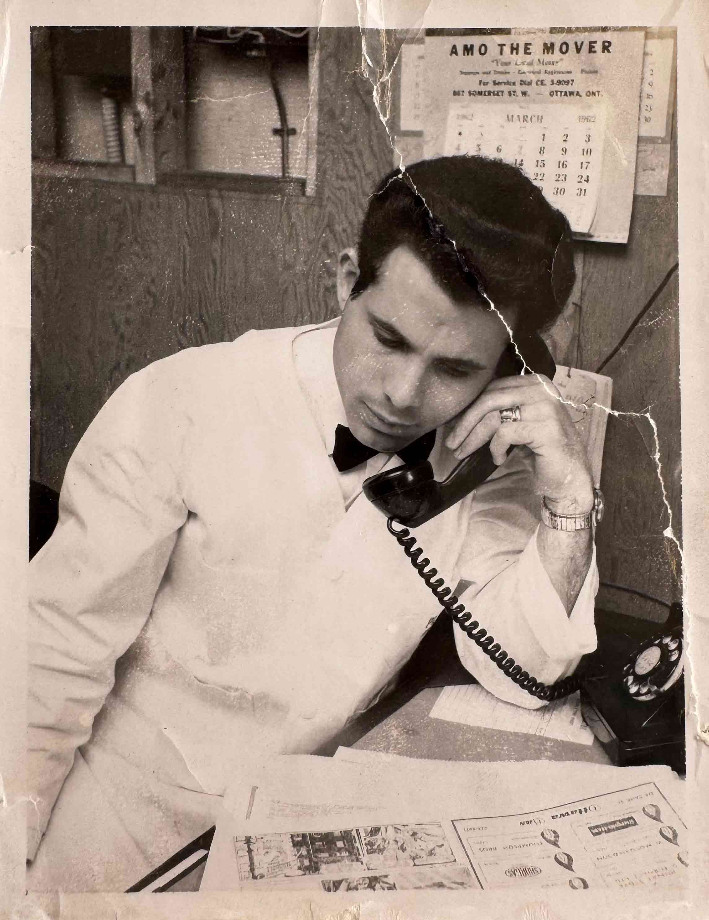 A black and white photo of a Greek man working and talking on the phone.