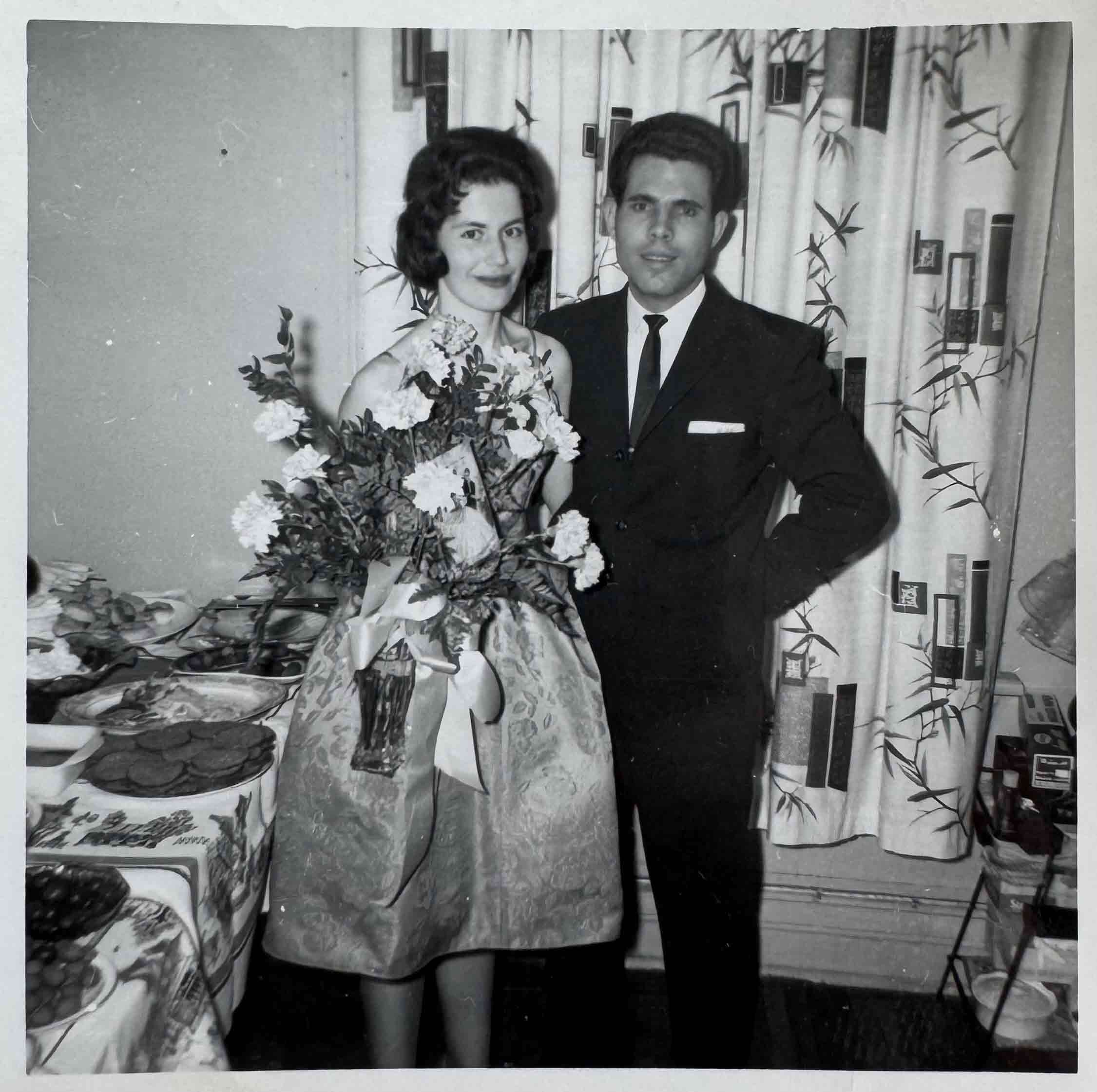 A black and white photo of Greek couple dressed formally with flowers.
