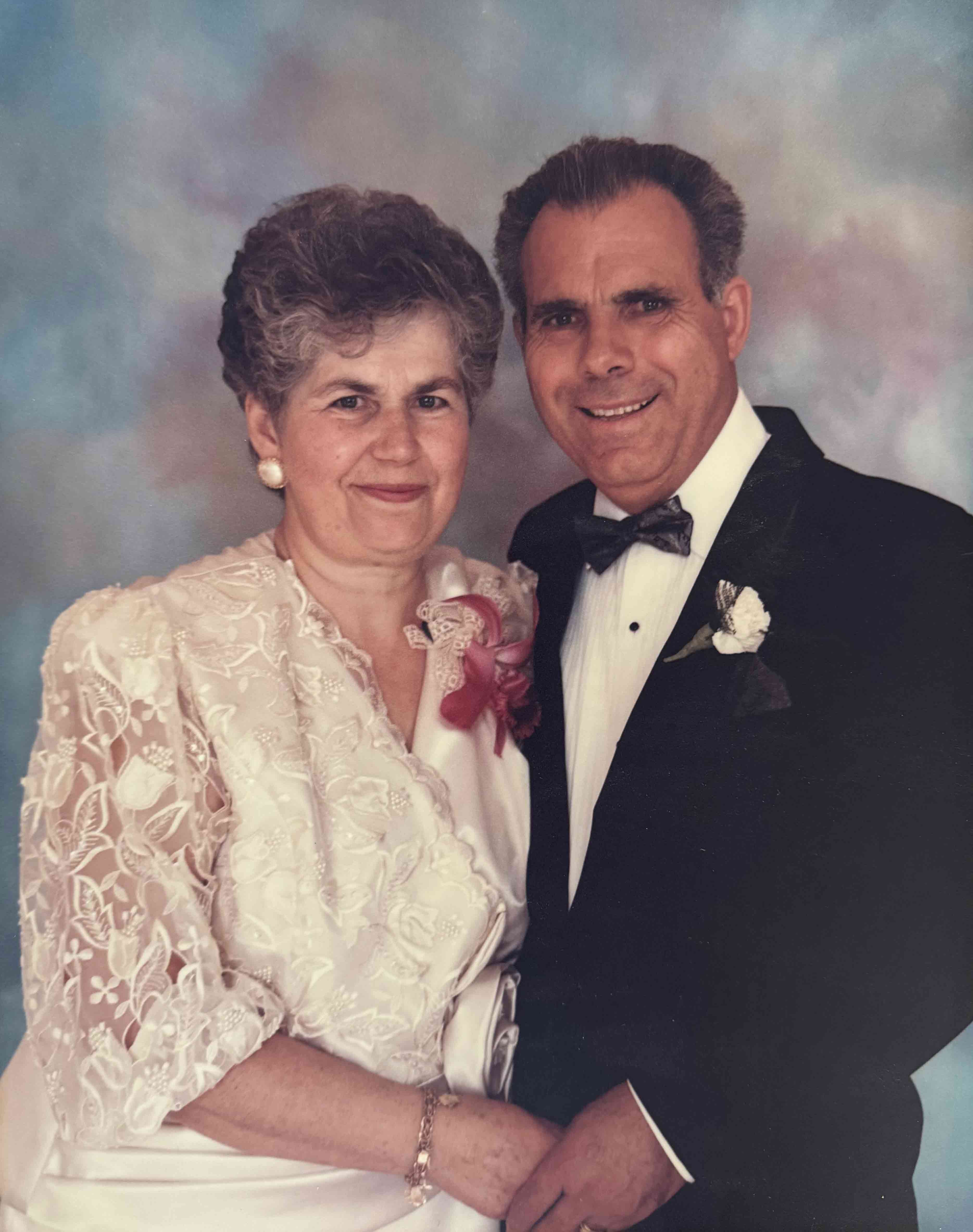 A portrait of a Greek couple dressed formally and smiling.