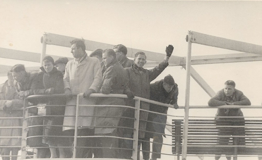 Black and white image of Abraham den Ouden and several European immigrants looking from a ship’s railing.
