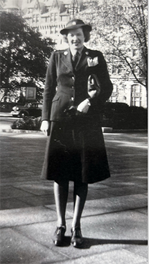 Black and white photo of a smiling white woman in uniform, standing outside of a large building.