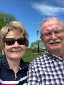 An older white woman and man outdoors with trees and green grass behind them.