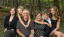 A portrait of a white family, including two children with their arms wrapped around adults, sitting outdoors.