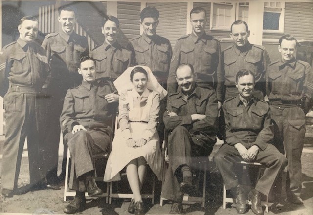 Sepia photo of a group of smiling uniformed men, and one woman in nurse’s clothing. 