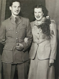 Sepia portrait of a white woman linking her arm through a man’s, both dressed formally.